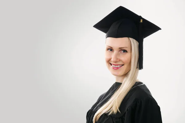 Absolvent univerzity nosit čepici a šaty na šedém pozadí — Stock fotografie