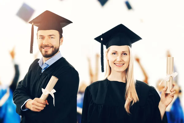 Happy graduates with diplomas wearing gowns at graduation ceremo — Stock Photo, Image
