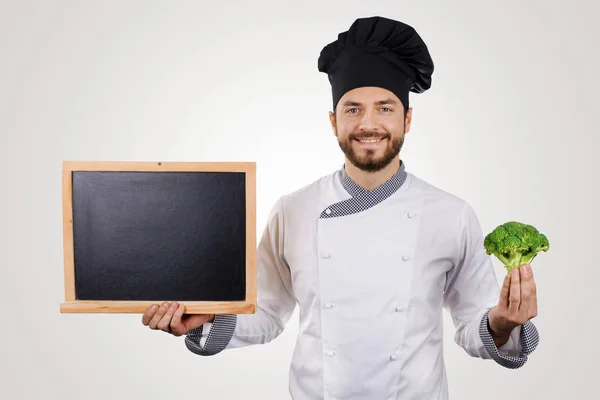 Jovem chef sorridente com quadro-negro em branco e brócolis na mão — Fotografia de Stock