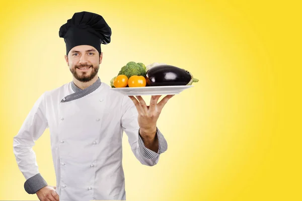 Cozinhar segurando prato de legumes no fundo amarelo. espaço de cópia — Fotografia de Stock