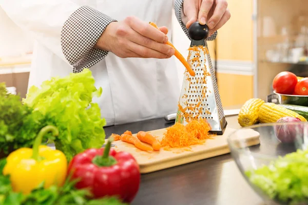 Koch schreddert Möhren mit Reibe in Küche — Stockfoto