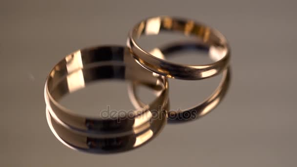 Dos anillos de boda de oro girando en la superficie del espejo — Vídeos de Stock