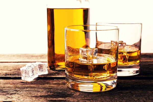 Vasos de whisky y botella en mesa de madera contra fondo blanco — Foto de Stock