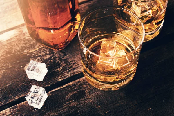 Botella de whisky y vasos con cubitos de hielo en la vieja mesa de madera — Foto de Stock