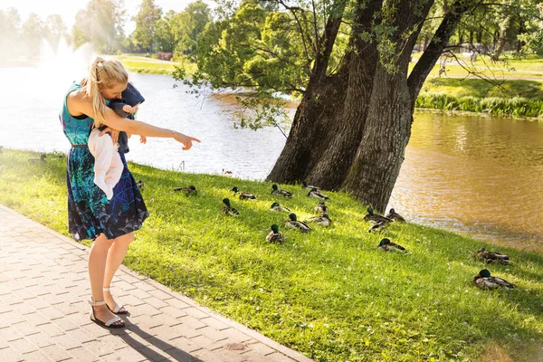 公園の池の近くの彼女の赤ちゃんにアヒルを示す母 — ストック写真