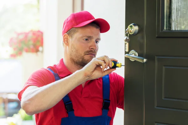 Cerrajero en uniforme rojo instalando nueva cerradura de la puerta de la casa — Foto de Stock