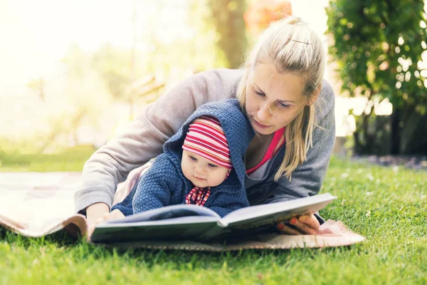 Mãe lendo um livro para bebê no jardim do quintal em cobertor — Fotografia de Stock