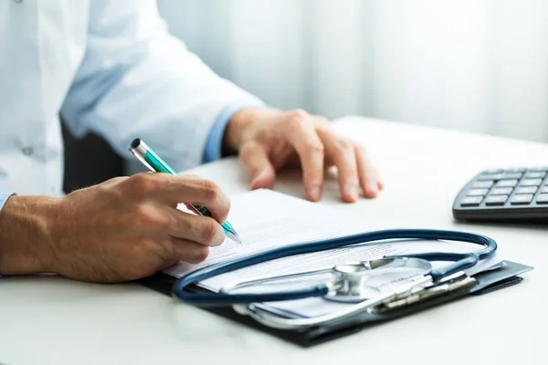 Médico que escreve a prescrição na mesa no escritório das clínicas — Fotografia de Stock