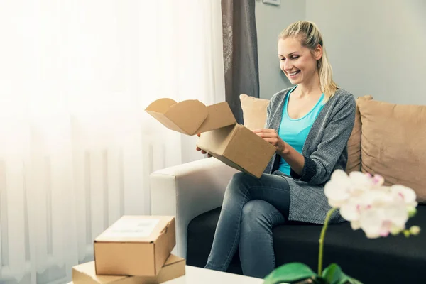 Доставка на дом - улыбающаяся молодая женщина открывает картонную коробку — стоковое фото
