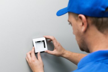 Elektrikçi mavi üniformalı duvarda ışık anahtarı yükleme