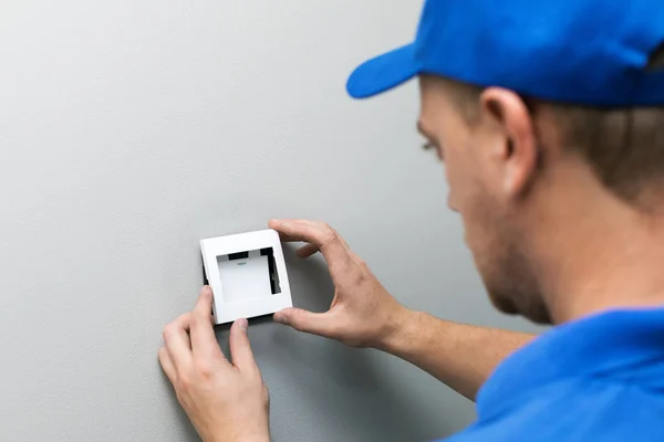 Elektricien in blauwe uniform installeren lichtschakelaar op de muur — Stockfoto