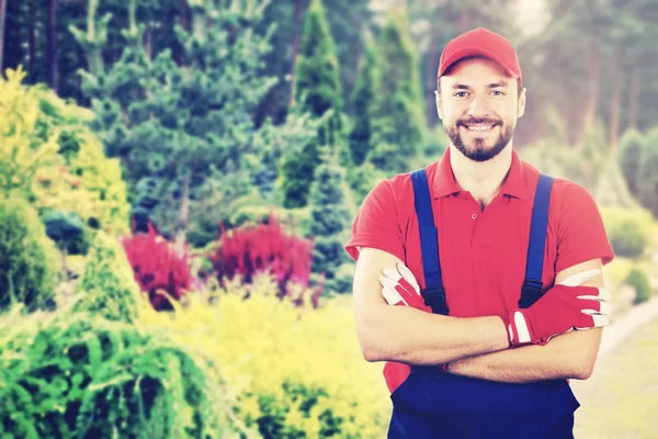 Joven jardinero sonriente con brazos cruzados de pie en el jardín — Foto de Stock