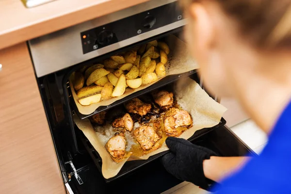 Mulher preparando batatas e carne de frango no forno em casa cozinha — Fotografia de Stock