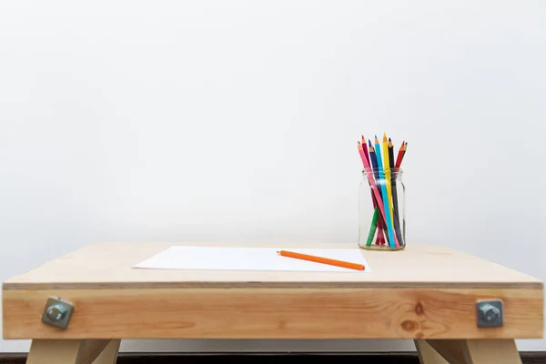 Houten kind tekenen van de tabel met kleur potloden door de witte muur — Stockfoto