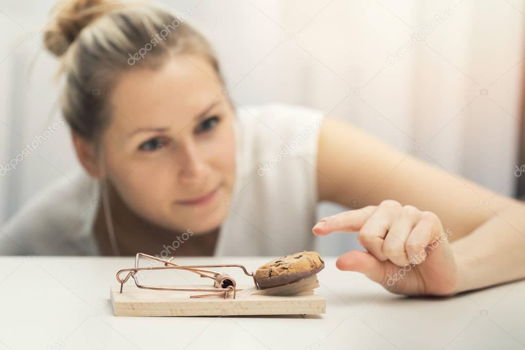 hungry woman trying to steal cookie from mouse trap. weight loss diet plan concept