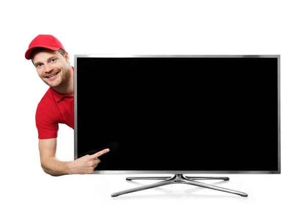 Smiling young man in red uniform pointing on blank tv screen — Stock Photo, Image