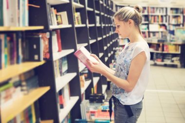kitapçıda satın almak için bir kitap seçerek genç kadın