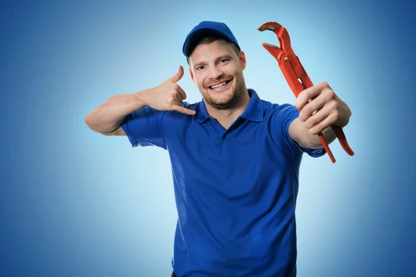 Servicios de fontanería - fontanero con llave que muestra el gesto de llamada telefónica sobre fondo azul — Foto de Stock