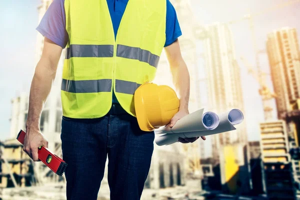 Építőmérnök, biztonsági mellény és blueprint tekercs a kezében: építési telek — Stock Fotó