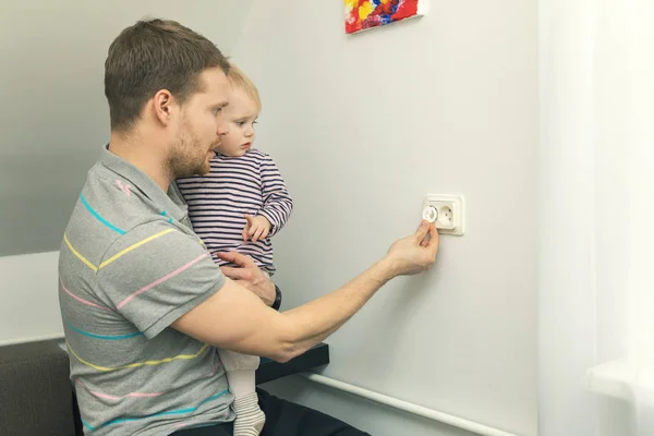 子供の安全家庭で。電気による損傷から子供を保護するために世話をする父 — ストック写真