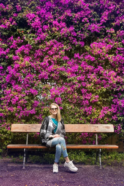 woman sitting on bench in front of purple flower hedge