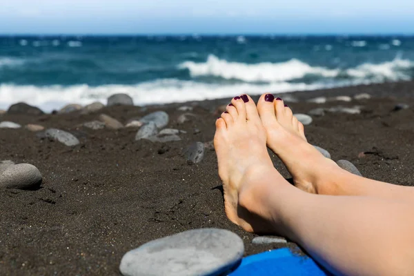 Sola - kvinna fötterna på svarta sandstranden — Stockfoto