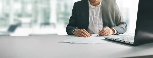 Young man in suit writing business papers at desk in modern cowo — ストック写真