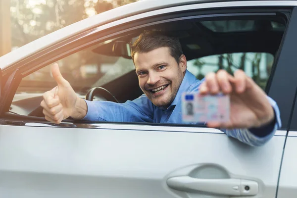 Jonge glimlachende man zitten in de auto en tonen zijn nieuwe bestuurder — Stockfoto