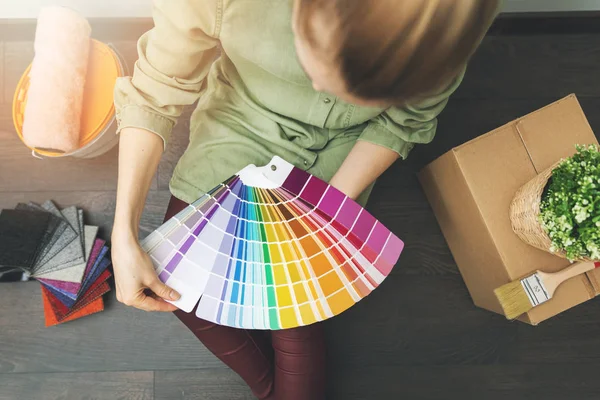 Mujer sentada en el suelo en la habitación y eligiendo el color de pintura de la muestra para el nuevo diseño de interiores — Foto de Stock