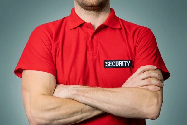 security service guard in red uniform standing on gray background with arms crossed