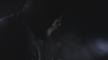 Siyah kapüşonlu adam karanlık odada elektronik sigara içiyor.