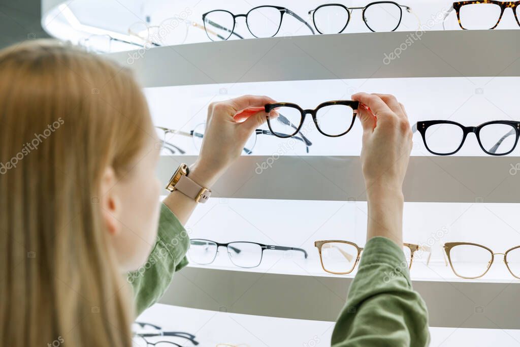 woman pick a eyeglasses from shelf in optics store