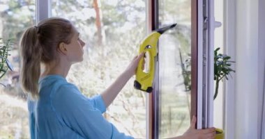 Kadın camları elektrikli süpürgeyle temizliyor.