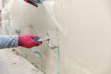 İnşaat işçisi duvara fiberglas alçı örgüsü yerleştiriyor.