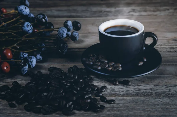 Café chaud en tasse noire avec des grains de café et des fleurs disposées o — Photo