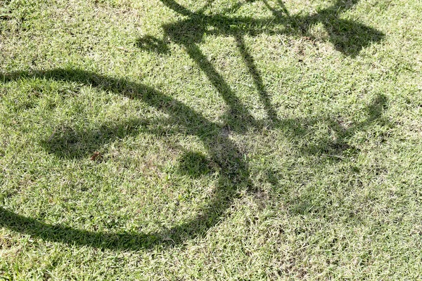 The shadow of a bicycle on a lawn.