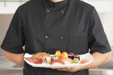 Male chef holding a plate full of sushi clipart