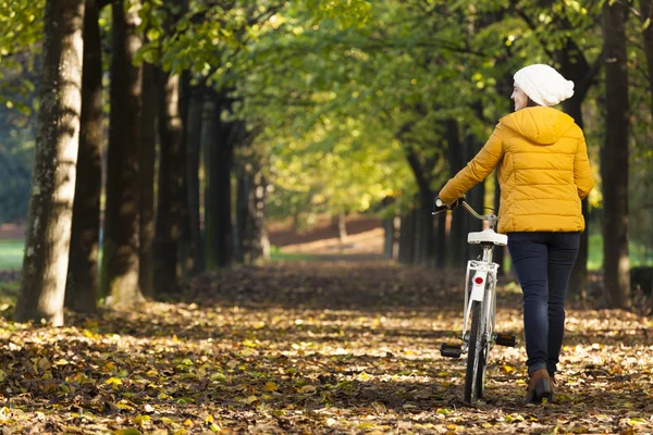 Kvinnan promenader med cykel i höst park — Stockfoto