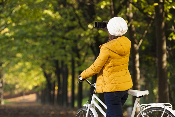 Flicka på cykel tar bilder med mobilen på park — Stockfoto