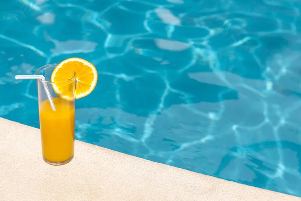 Glass of orange juice in the edge of swimming pool — Stock Photo, Image
