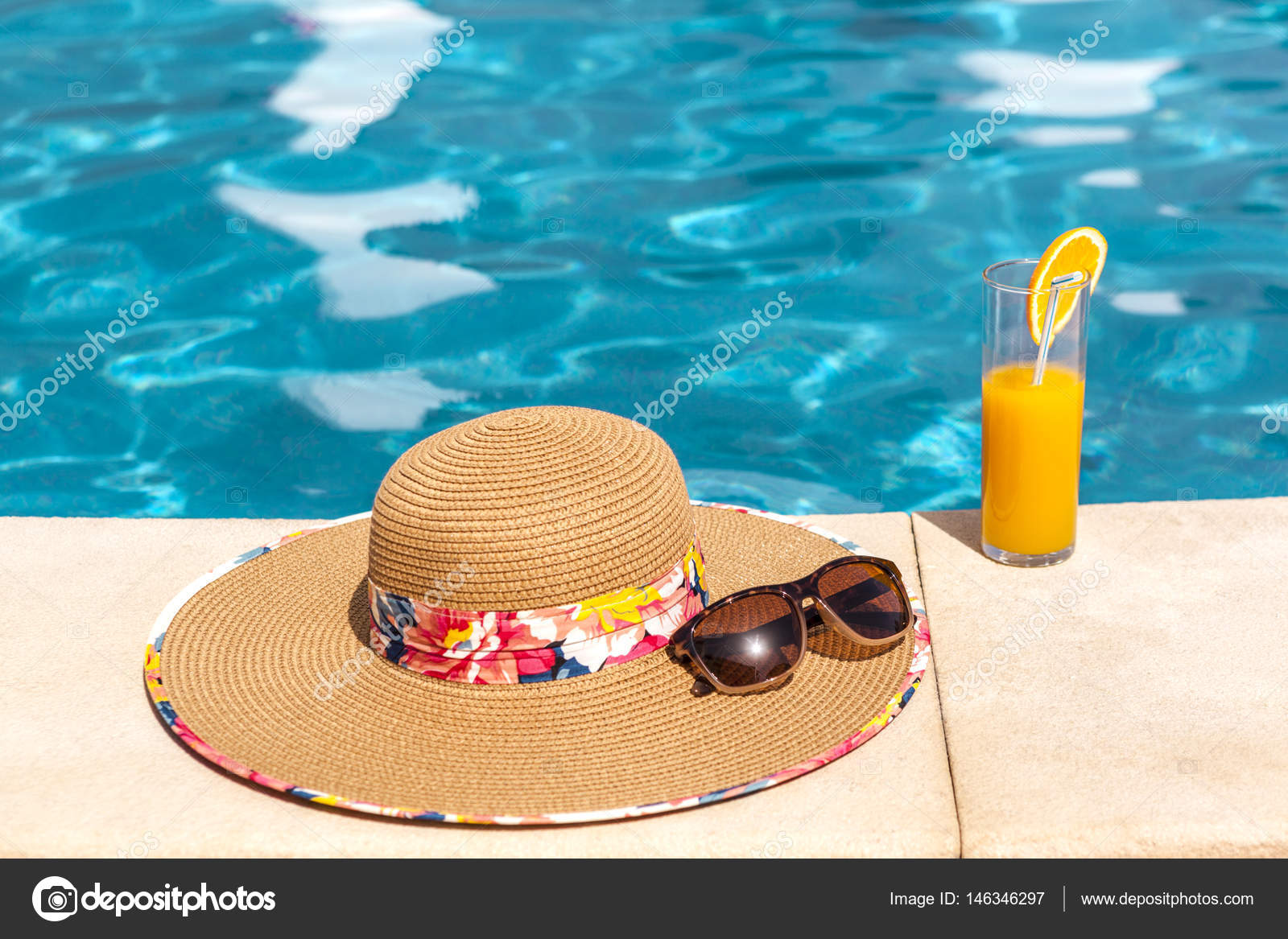 Beach hat, orange juice and sunglasses near the swimming pool