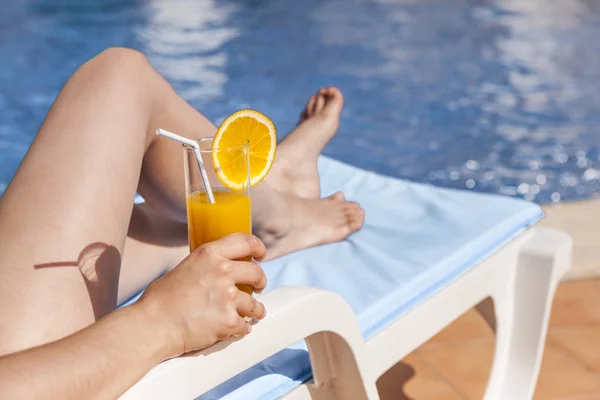 Main de femme avec jus d'orange près de la piscine — Photo