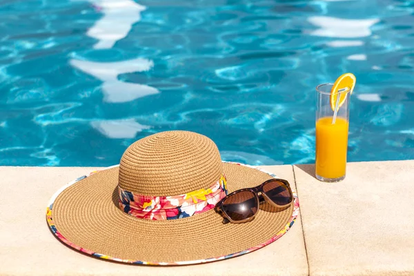 Beach hat, orange juice and sunglasses near the swimming pool — Stock Photo, Image