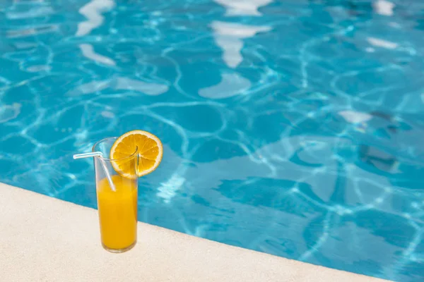 Glass of orange juice with orange slice on the edge of swimming pool — Stock Photo, Image