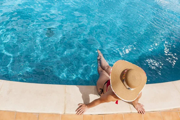 Mulher de chapéu sentada à beira da piscina — Fotografia de Stock