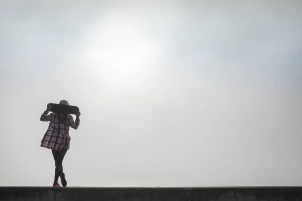 Девушка стоит со скейтбордом и смотрит на море — стоковое фото
