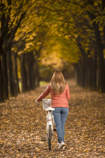 Kvinnan promenader med cykel i höst park — Stockfoto