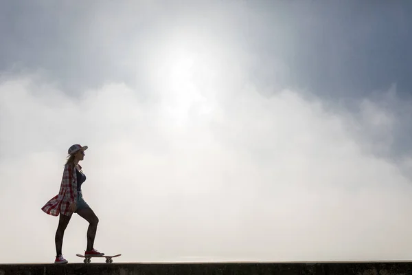 ビーチそばのスケート ボードに乗ってかわいい女の子のシルエット — ストック写真