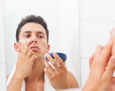 Yüzünü krem uygulamak ve kendisi de süre ayna önünde duran seyir gömleksiz adam