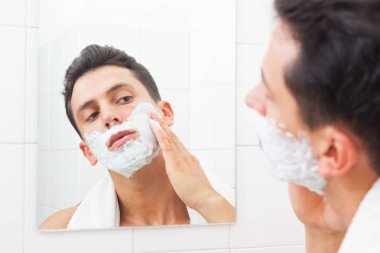 Havlu banyoda yüzüne traş köpüğü koyarak yakışıklı adam